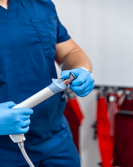 Manos con guantes azules sostienen un endoscopio antes de un procedimiento.
